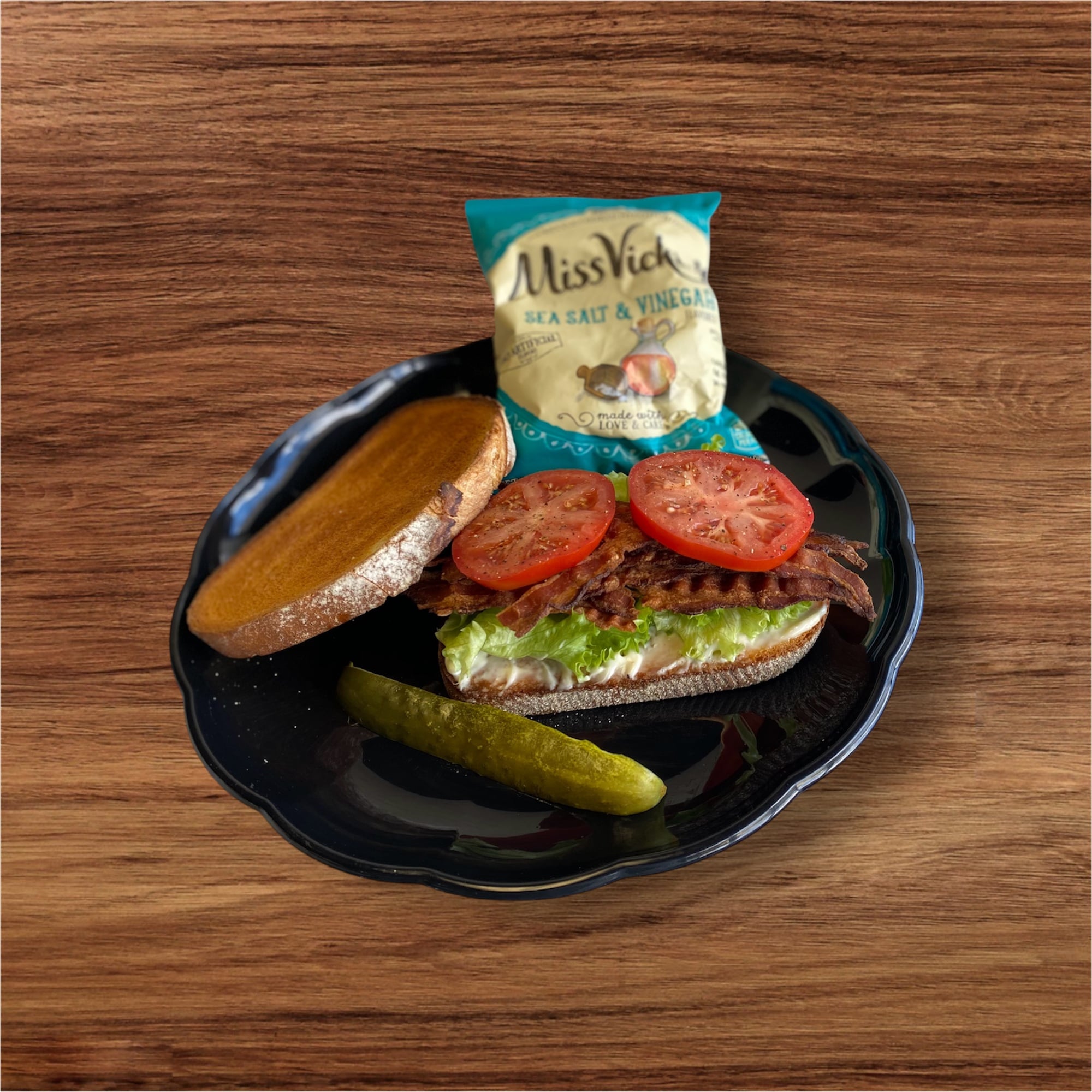 Classic BLT sandwich with kettle chips and a pickle on a black plate