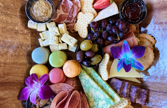 Classic charcuterie box with meats, cheeses, macarons, crackers, fruit, and olives