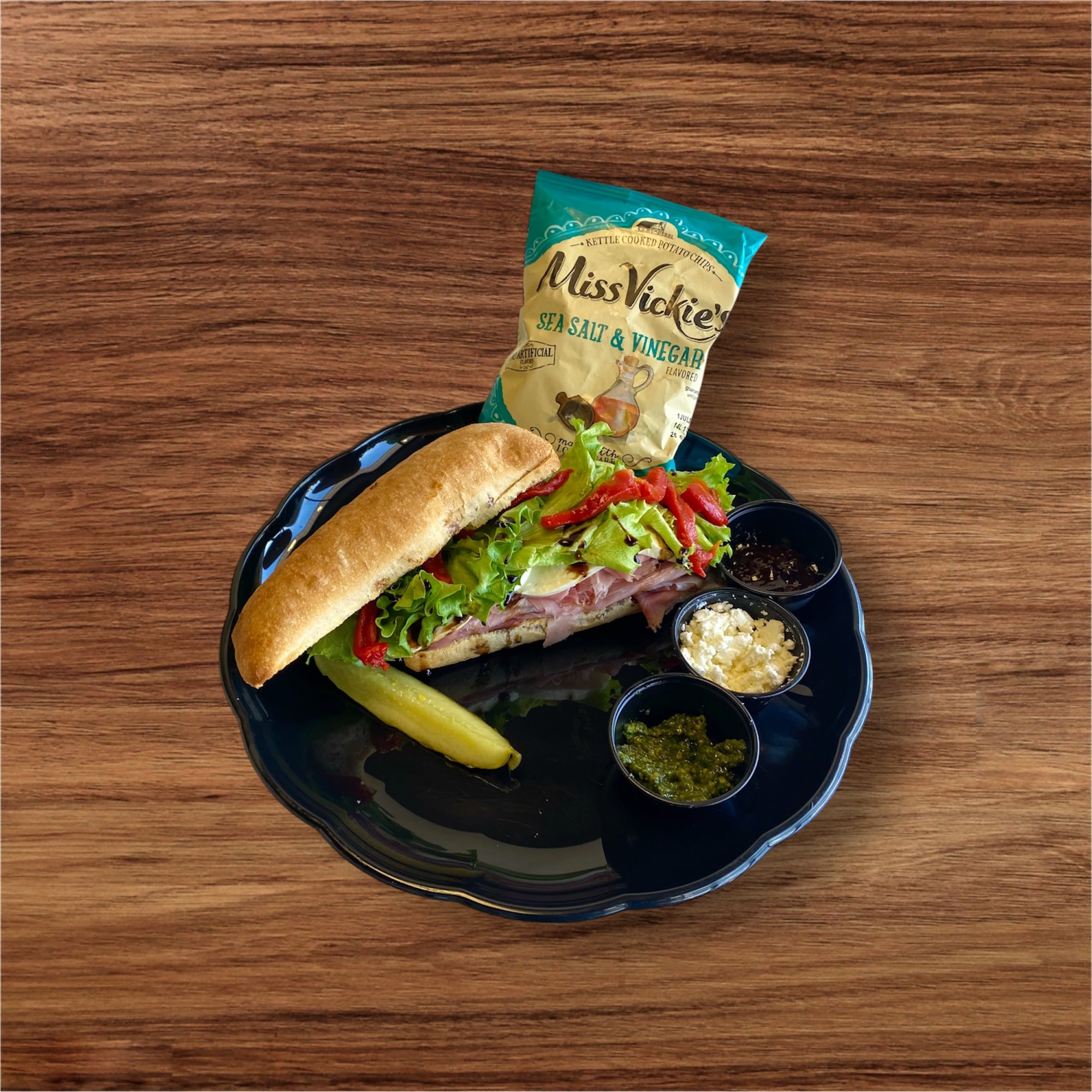 Italiano deli sandwich served with chips and pickle on black plate