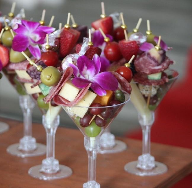 Individual charcuterie cups served in martini glasses with meat, cheese, fruit, and flowers