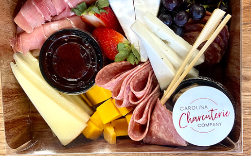 Mini charcuterie box with meats, cheeses, jam, and fruit, styled in a small container