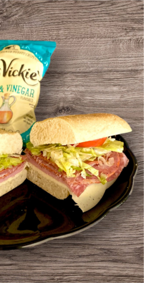 Close-up of The Goombah Italian sandwich on a black plate with sea salt chips