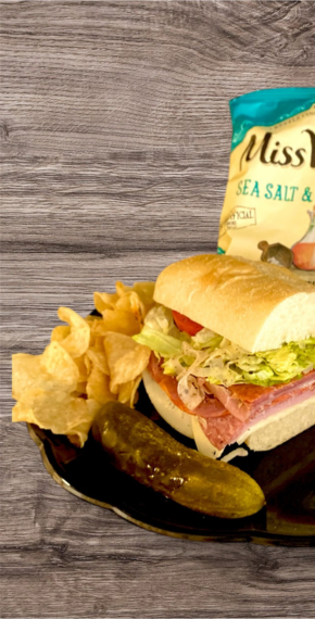 The Goombah Italian sandwich on a plate with potato chips and a pickle spear