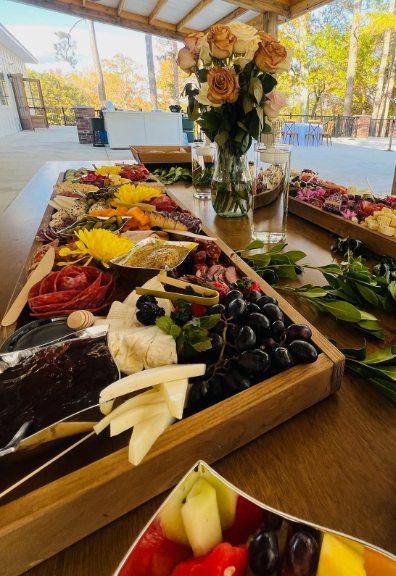 Close-up of an artisan charcuterie grazing table with meats, cheeses, and floral decor under a pavilion
